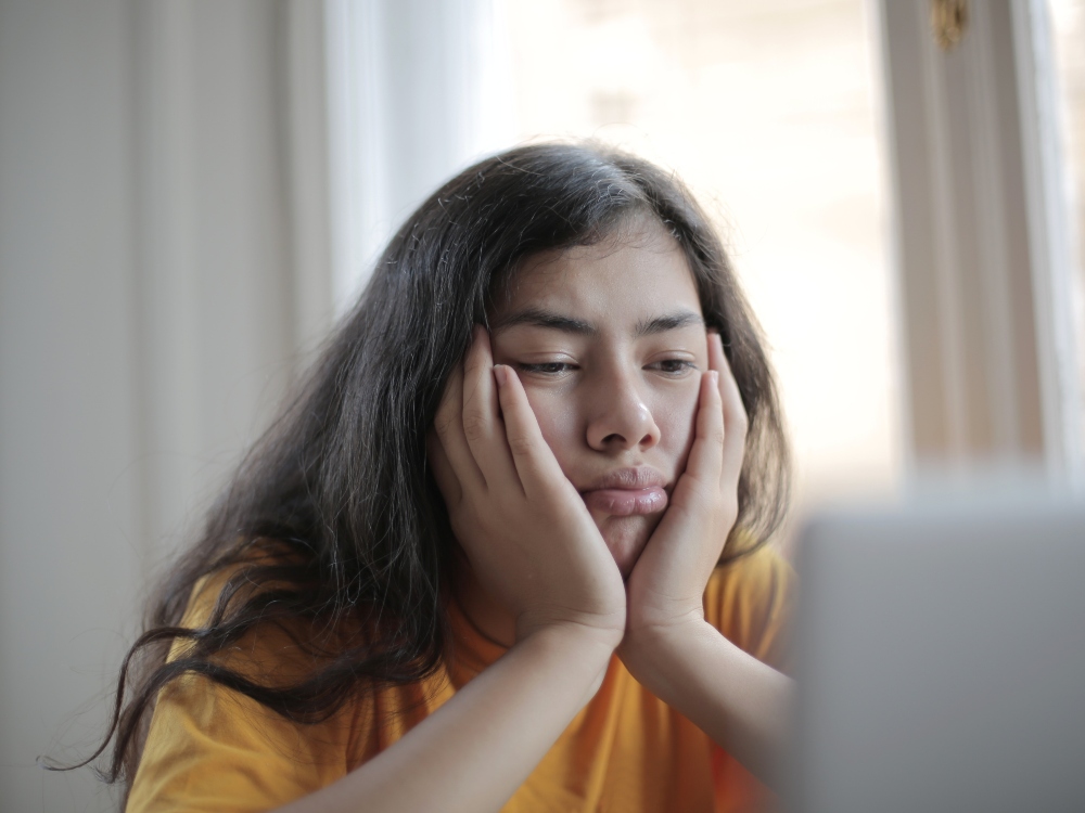 A teenage girl looking at a laptop, frustrated and unmotivated by schoolwork