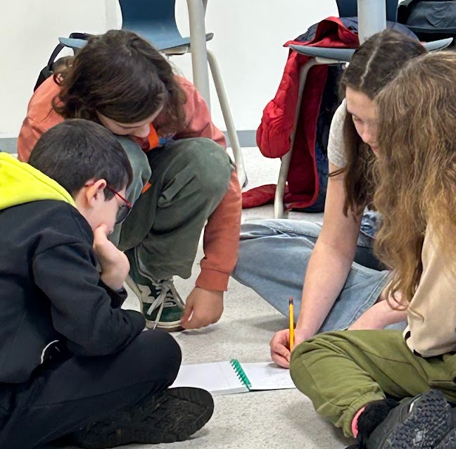 Three children sitting on the floor solving a problem together, writing in a notebook