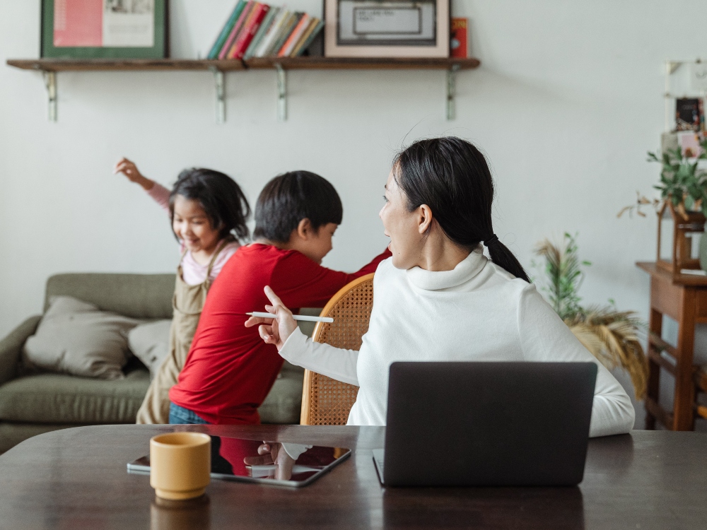 A parent who is trying to work but her two kids playing are interrupting her