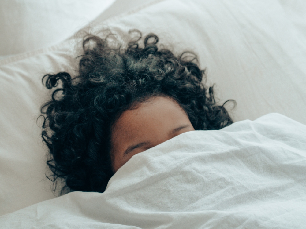 A child covered with a blanket in bed because he doesn't want to go to school